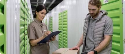 Storage facility staff reviewing inventory records on a tablet while inspecting stored goods and managing stock.