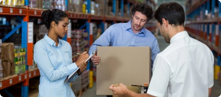 Warehouse team inspecting a cardboard package and checking inventory records to coordinate stock management and order fulfillment.